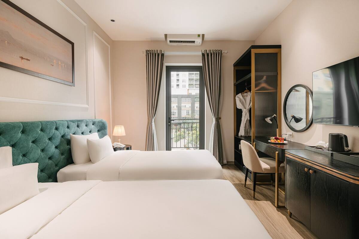 Habitación de hotel con dos camas, un escritorio, una silla, un armario y un gran ventanal con cortinas.
