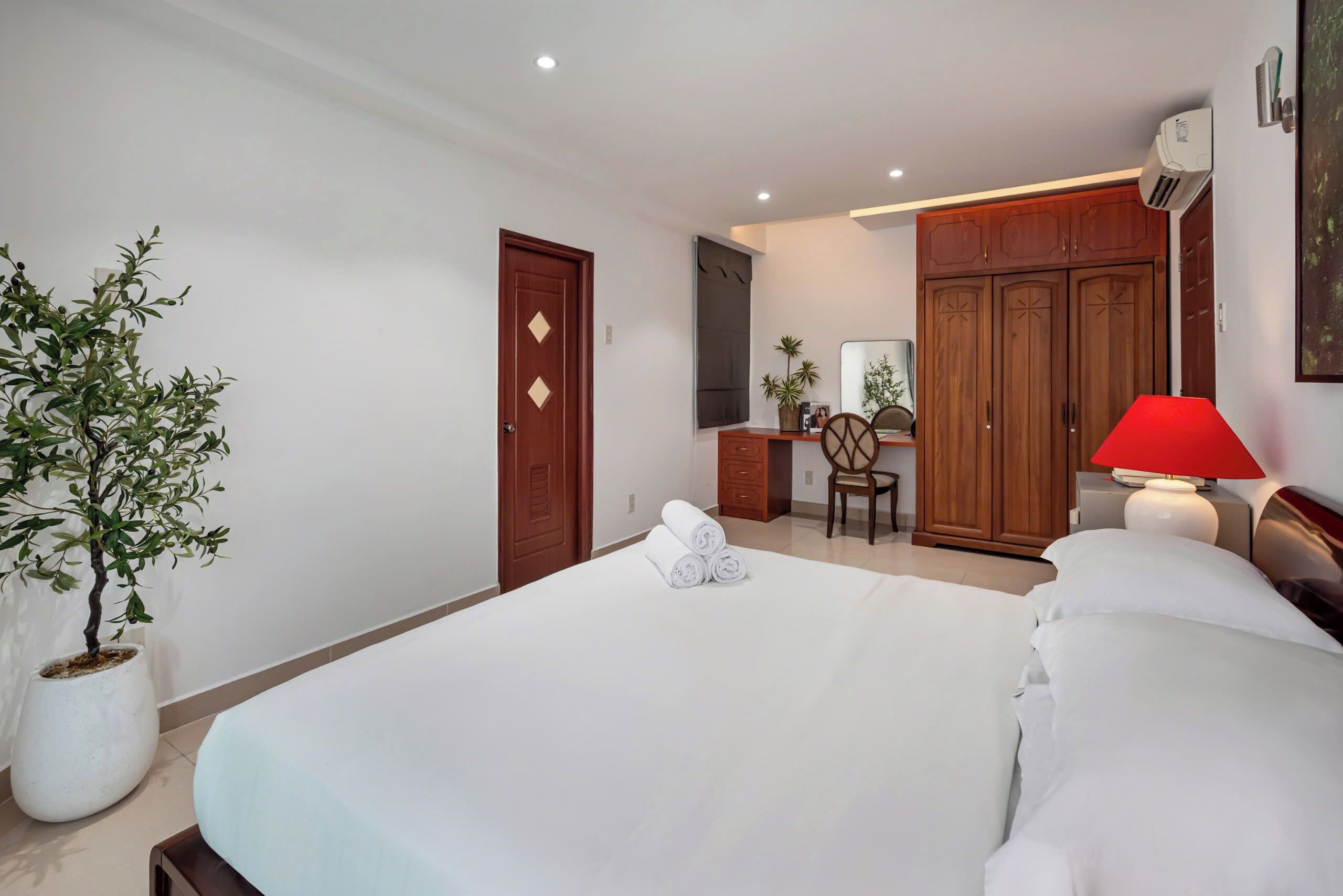 A hotel room with a bed, a desk, a chair, a wardrobe, and a potted plant.