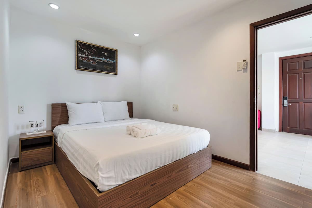 A neatly made bed in a room with a wooden headboard, a small bedside table, and a wall-mounted painting.