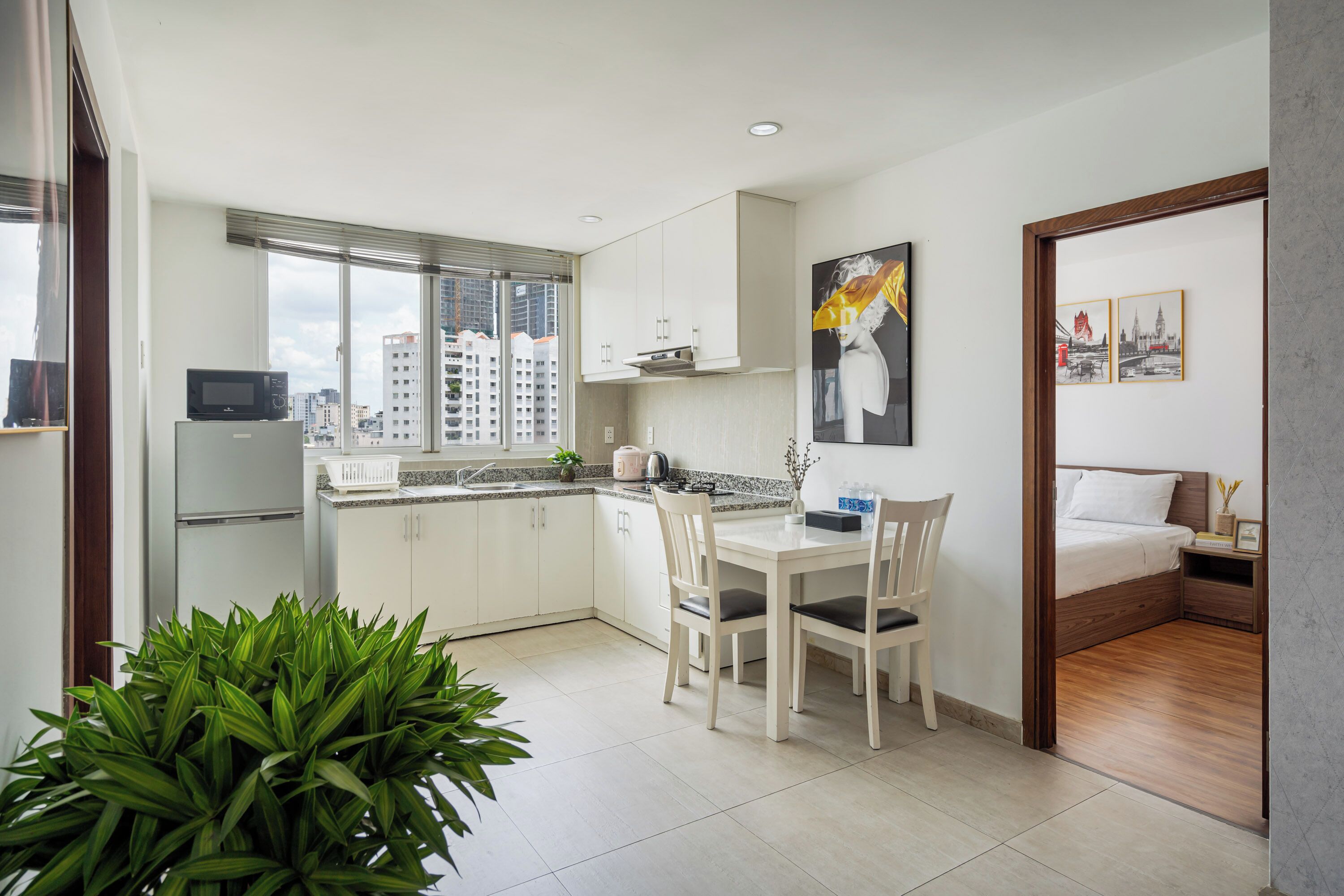 A modern kitchen with a refrigerator, microwave, and sink, a dining area with a table and chairs, and a bedroom with a bed and nightstand.