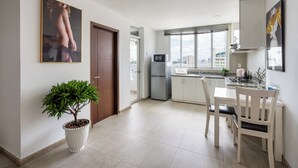 Une cuisine moderne avec des meubles blancs, un coin repas avec une table et des chaises blanches, une plante en pot et une vue sur la ville à travers de grandes fenêtres.
