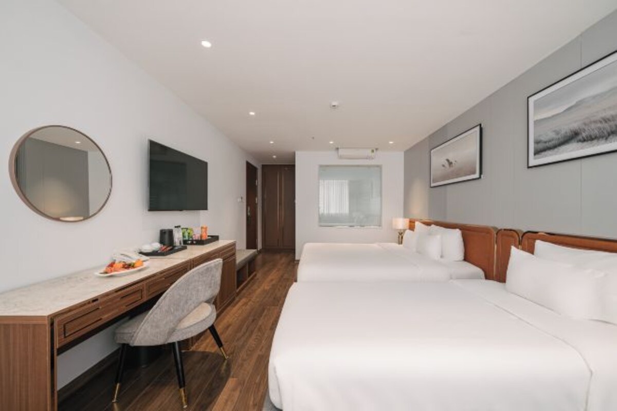 A hotel room with a desk, two beds, a chair, a TV, and artwork on the walls.