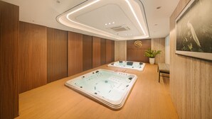 A spa room with two hot tubs, wooden panel walls, a ceiling light fixture, and a potted plant. - San Seize Hanoi Hotel (Hanoi)
