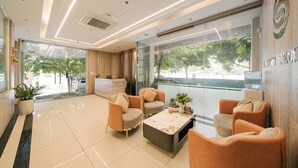 A modern lobby with a reception desk, seating area, and large windows offering a view of the outdoors. - San Seize Hanoi Hotel (Hanoi)