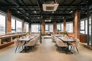 Un comedor moderno con paredes de ladrillo, ventanas amplias y varias mesas y sillas.