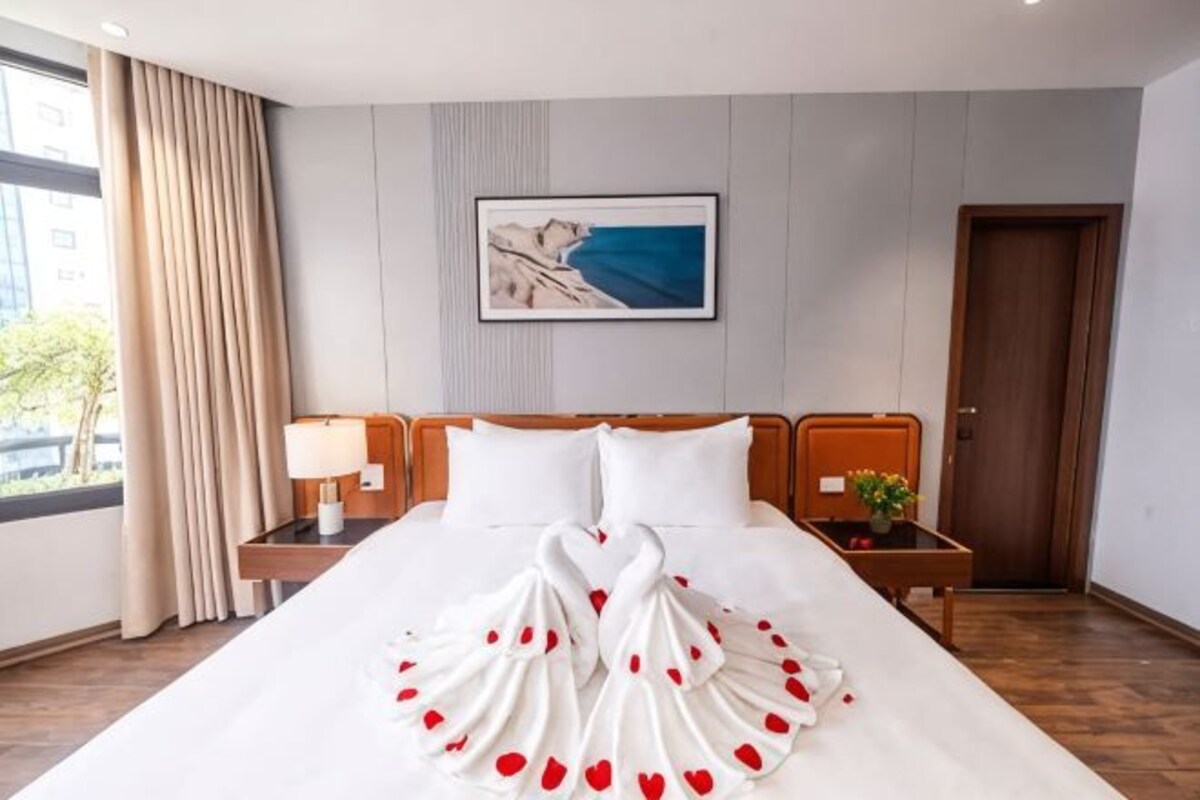 A hotel room with a large bed, a nightstand with a lamp, a framed picture on the wall, and a wooden door.