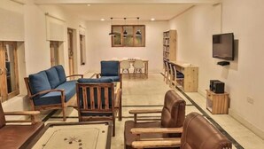 Een ruime woonkamer met een bank, stoelen, een salontafel, een eettafel en een boekenkast.