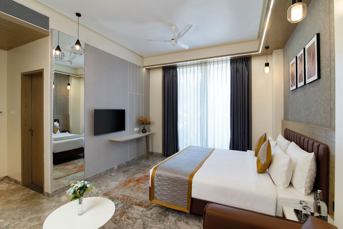 Une chambre d’hôtel avec un lit, une télévision, un miroir, une table ronde ornée d’un vase et un ventilateur de plafond.