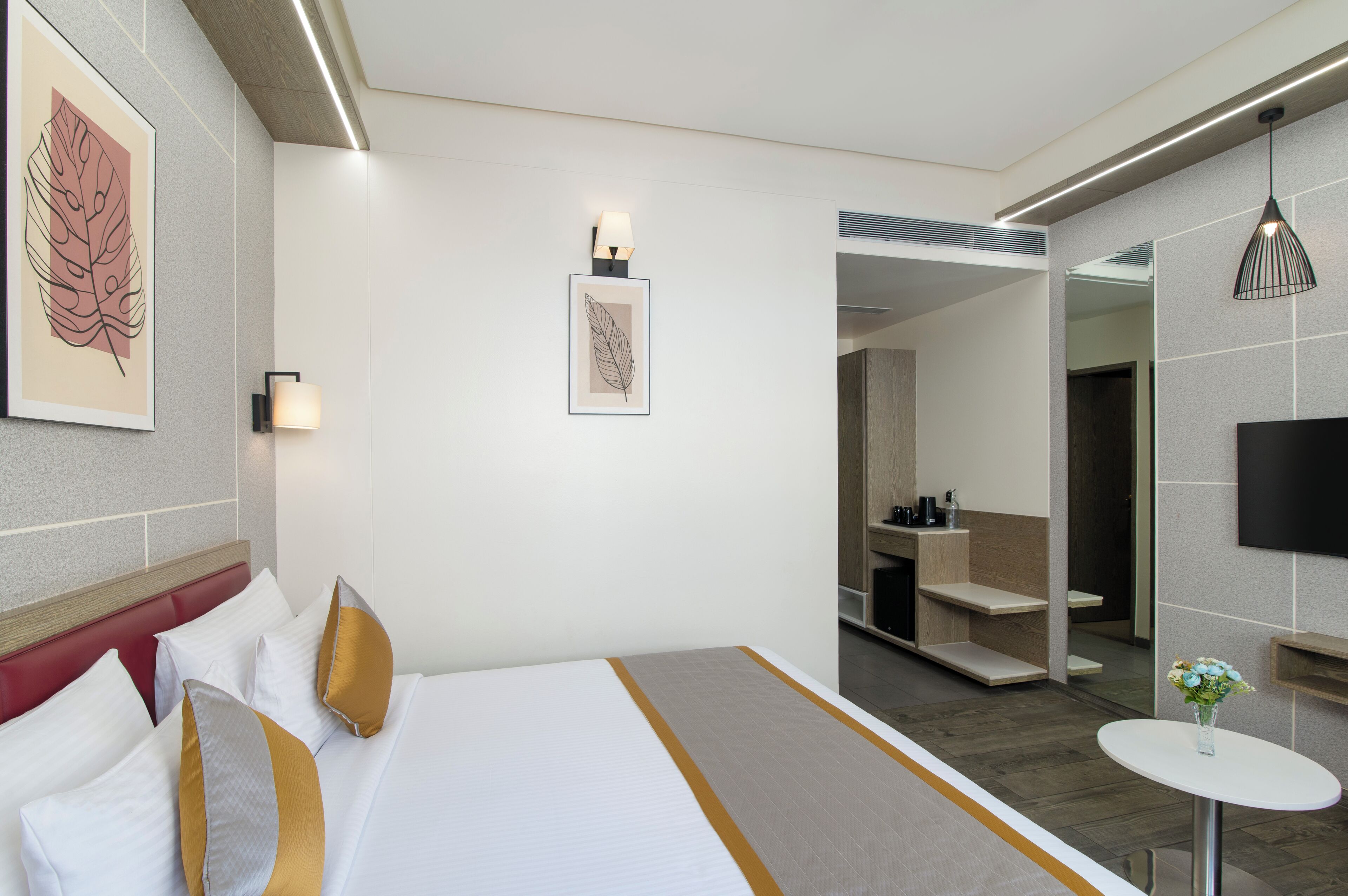 A hotel room with a bed, bedside tables, a mirror, a TV, and artwork on the walls.