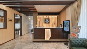 Un espace d’accueil d’hôtel comprenant un comptoir de réception en bois, un écran numérique et un coin salon.