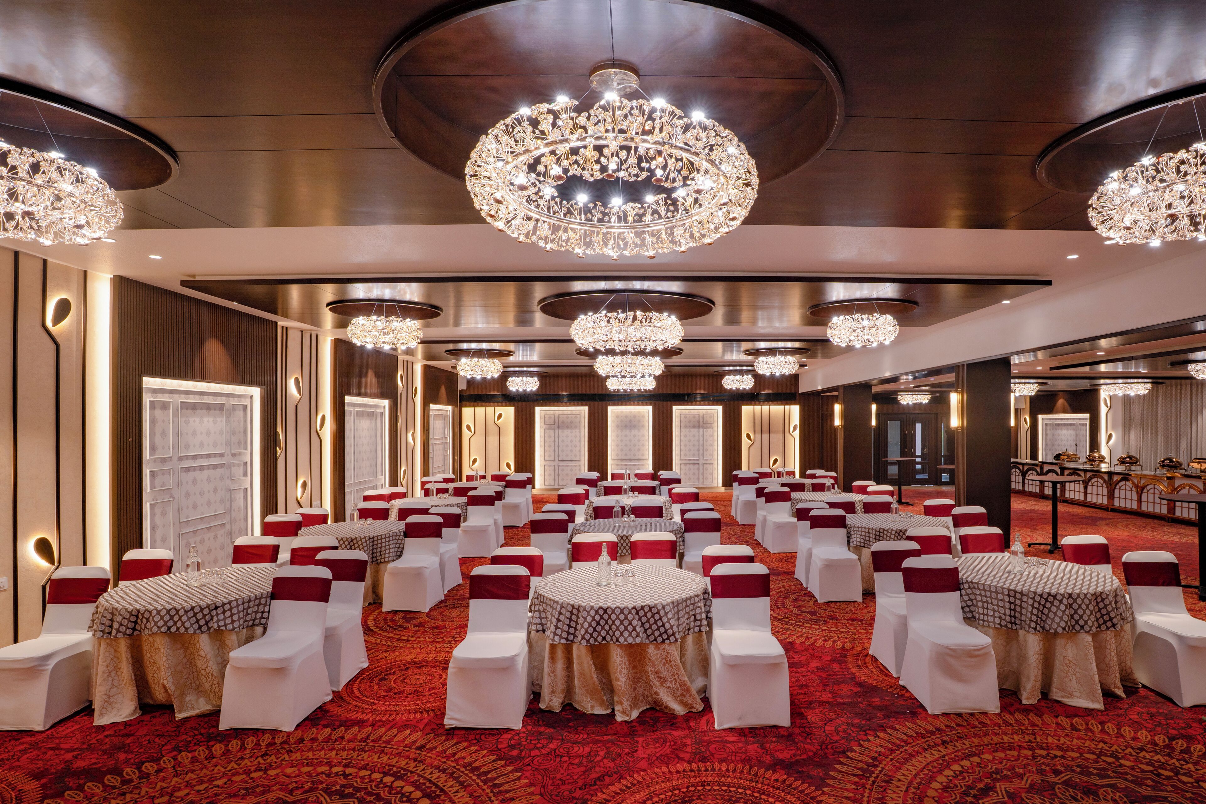 Un salón de banquetes con mesas redondas, sillas blancas y cintas rojas.