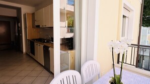 A kitchen with white cabinets, a dining area with white chairs, and a balcony with a railing. - Bixio Leisure Flexrent - Abyssinia (Riccione)