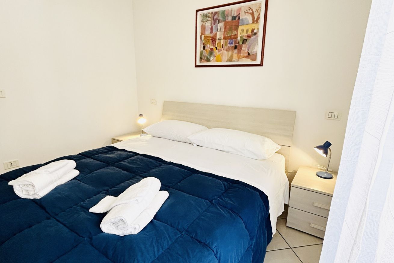 Une chambre d’hôtel avec un lit, deux serviettes blanches, une table de chevet, une lampe et un tableau au mur.