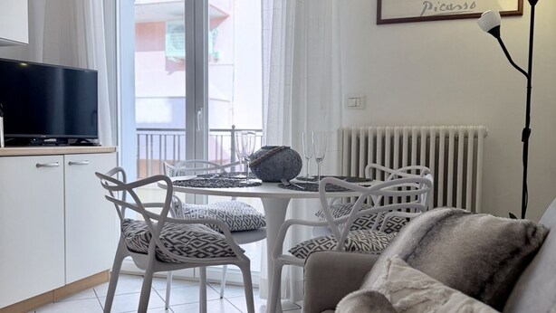 A modern living room with a sofa, a dining table with chairs, a TV on a cabinet, and a radiator. - Bixio Leisure Flexrent - Abyssinia (Riccione)