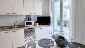 A modern kitchen with white cabinets, a microwave, a sink, and a window overlooking a balcony. - Bixio Leisure Flexrent - Abyssinia (Riccione)