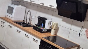 Een kleine keuken met witte kastjes, een houten aanrecht, een magnetron, een koffiezetapparaat en een zwarte oven.