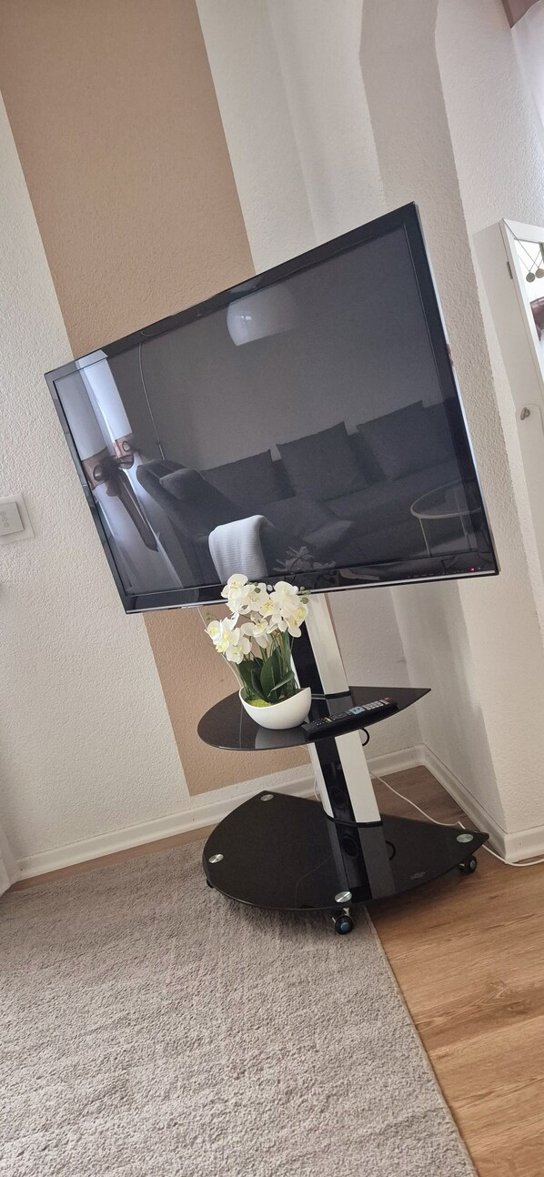Un televisor de pantalla plana sobre un pedestal negro con un florero blanco.