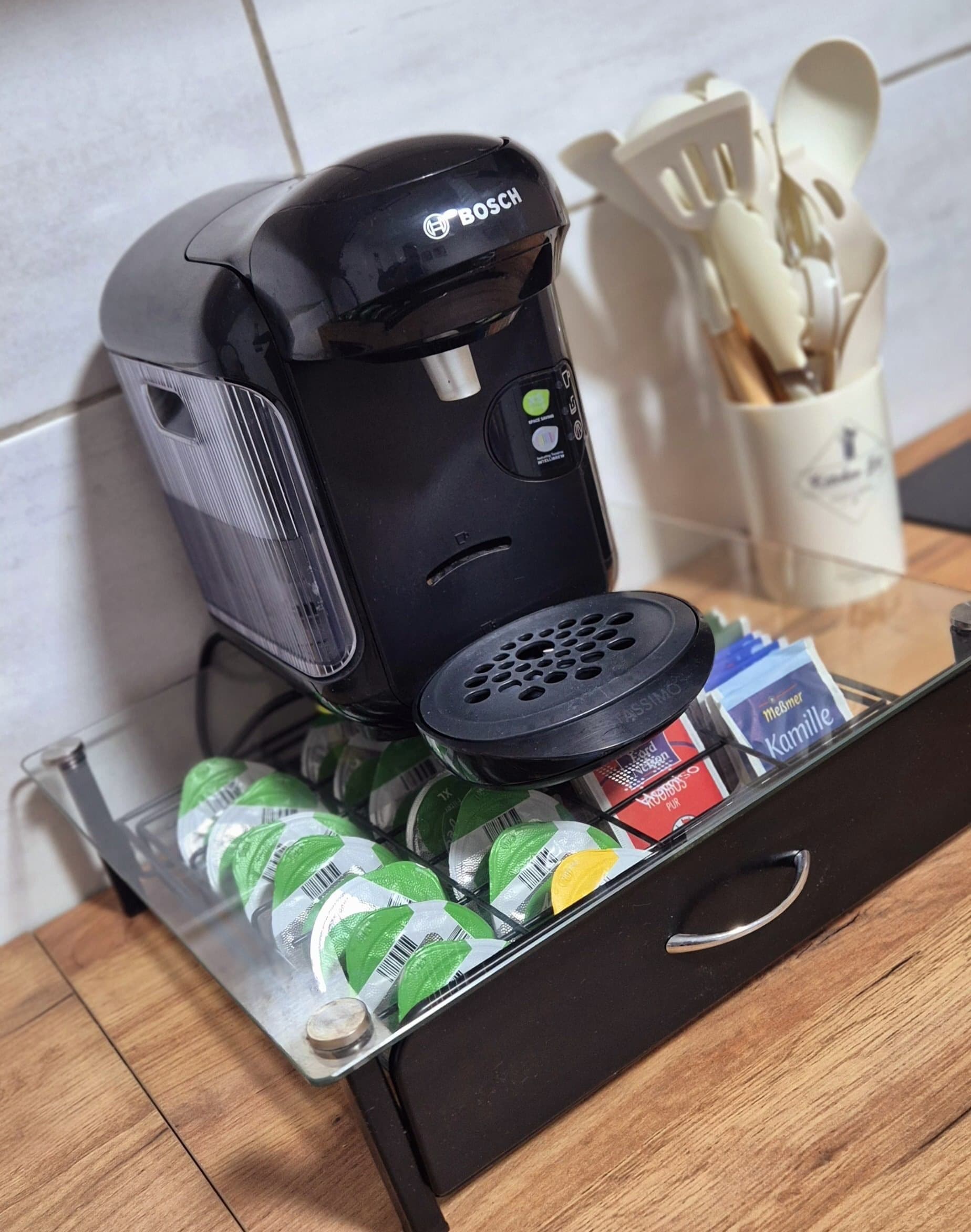 Eine Küchenzeile mit einer Bosch-Kaffeemaschine, einer Schublade voller Getränke und einem Utensilienhalter.