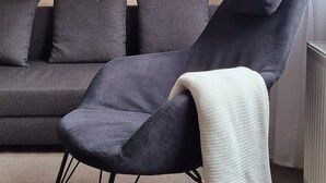 Een moderne woonkamer met een donkergrijze bank, een witte vloerlamp en een houten schommelstoel.
