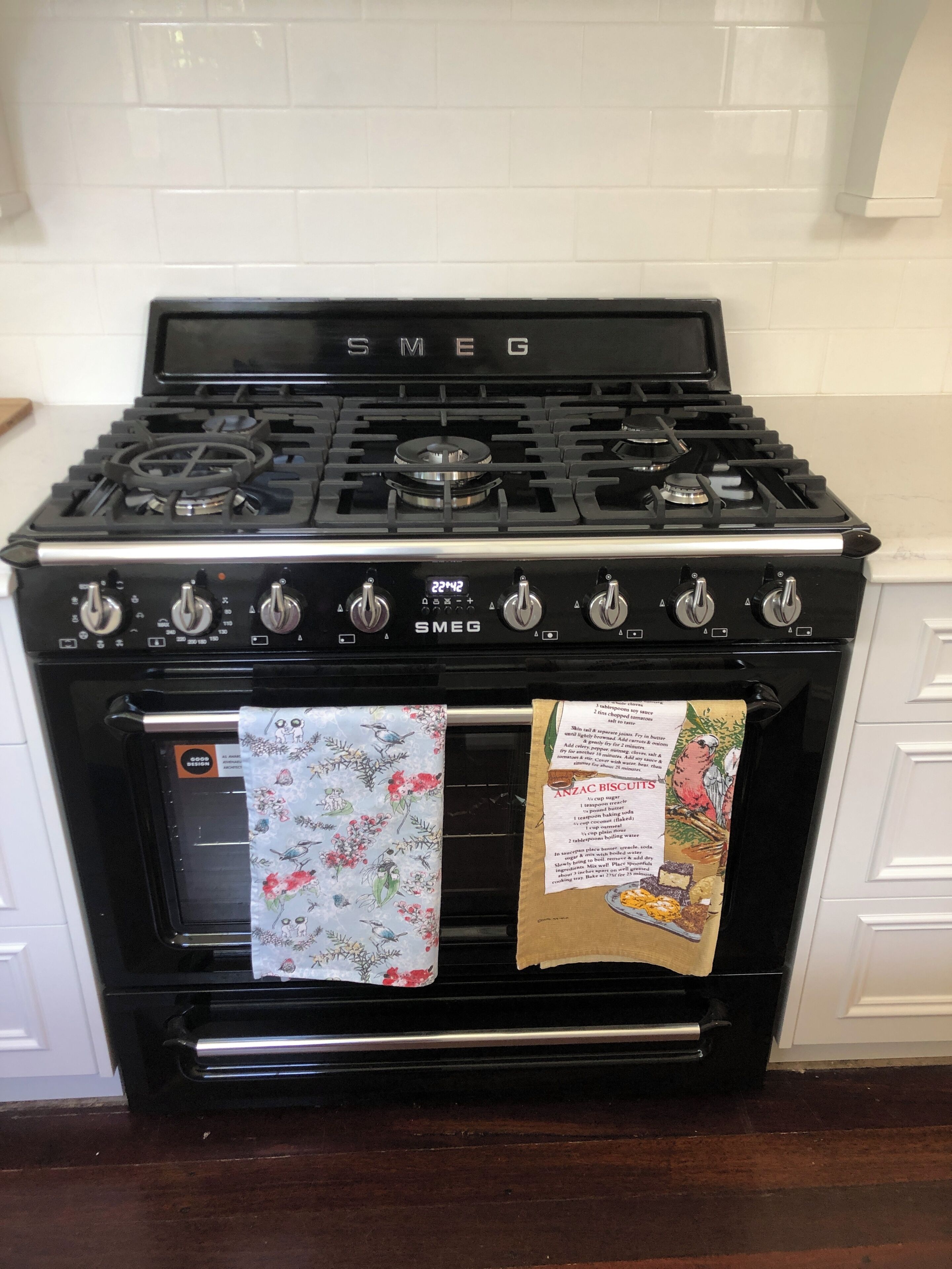 A black Smeg stove with a digital clock displaying 22:42, an oven, and a floral kitchen towel.