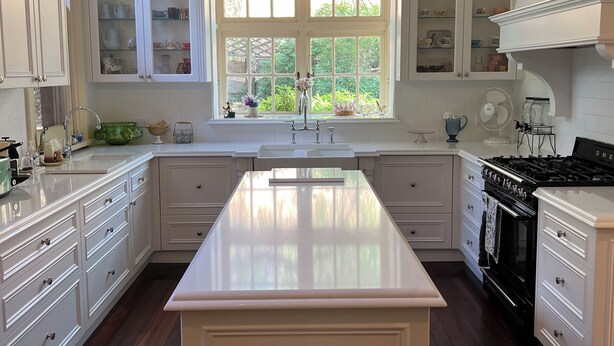 A spacious kitchen with white cabinetry, a central island, and a large window providing natural light. - Cosy and comfortable riverside homestead in Bridgetown - sleeps up to 14 guests. (Bridgetown)