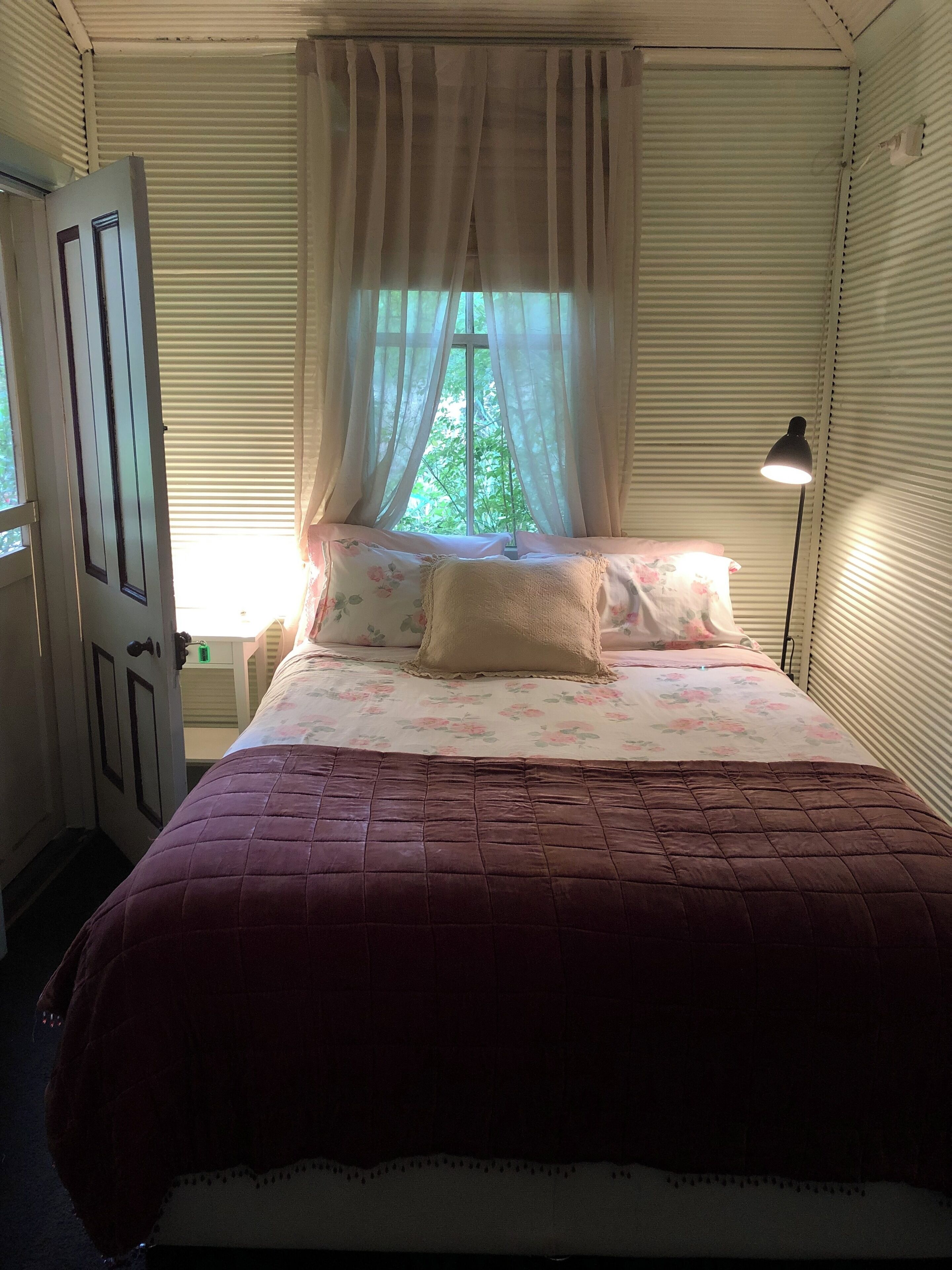 Une chambre à coucher avec un lit, une fenêtre avec des rideaux, une lampe de chevet et une porte.