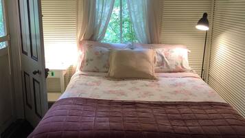 Une chambre à coucher avec un lit, une fenêtre avec des rideaux, une lampe de chevet et une porte.