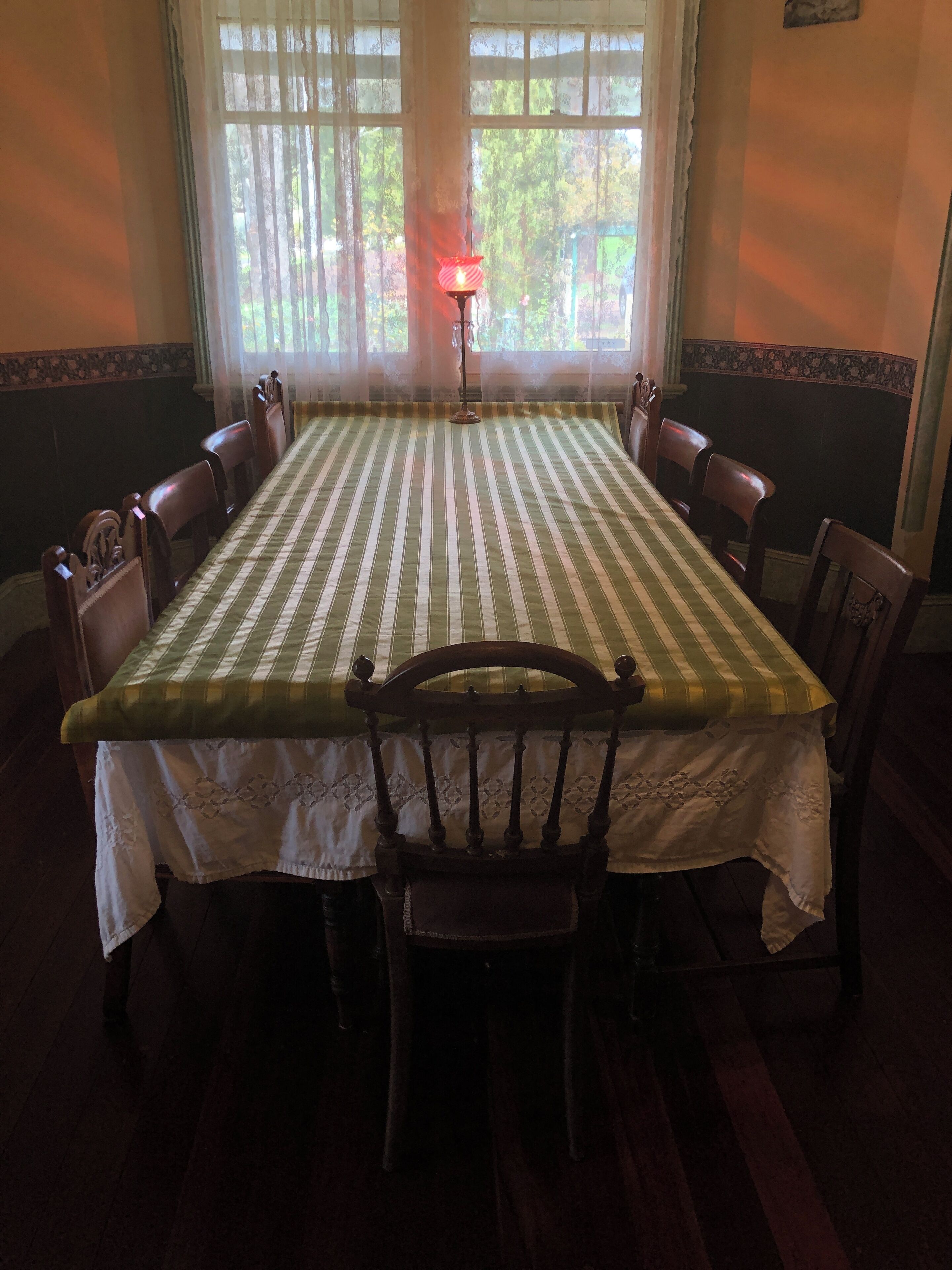 Uma sala de jantar com uma mesa posta para seis pessoas, rodeada por cadeiras de madeira.