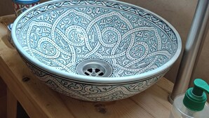 Un bany amb un lavabo decoratiu, un aixeta i una ampolla de desinfectant per a les mans sobre una prestatgeria de fusta.