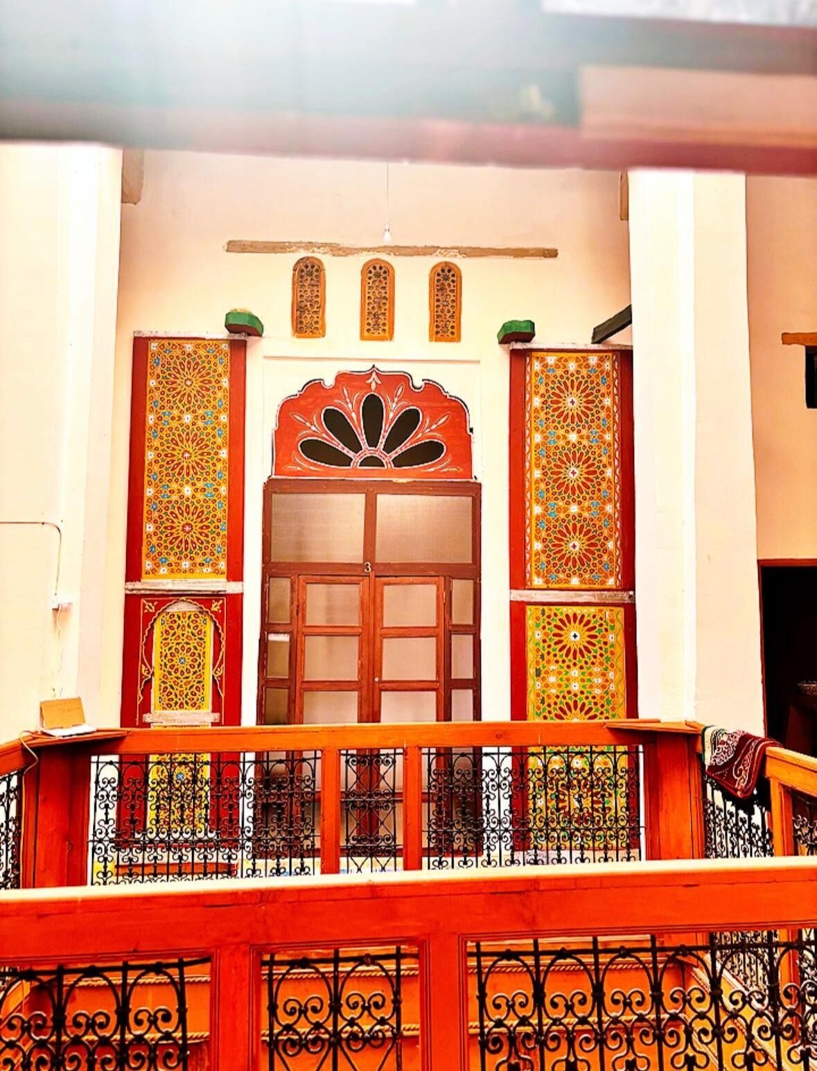 Fachada de um edifício tradicional com portas de madeira ornamentadas, painéis decorativos e varanda com grades de ferro forjado.