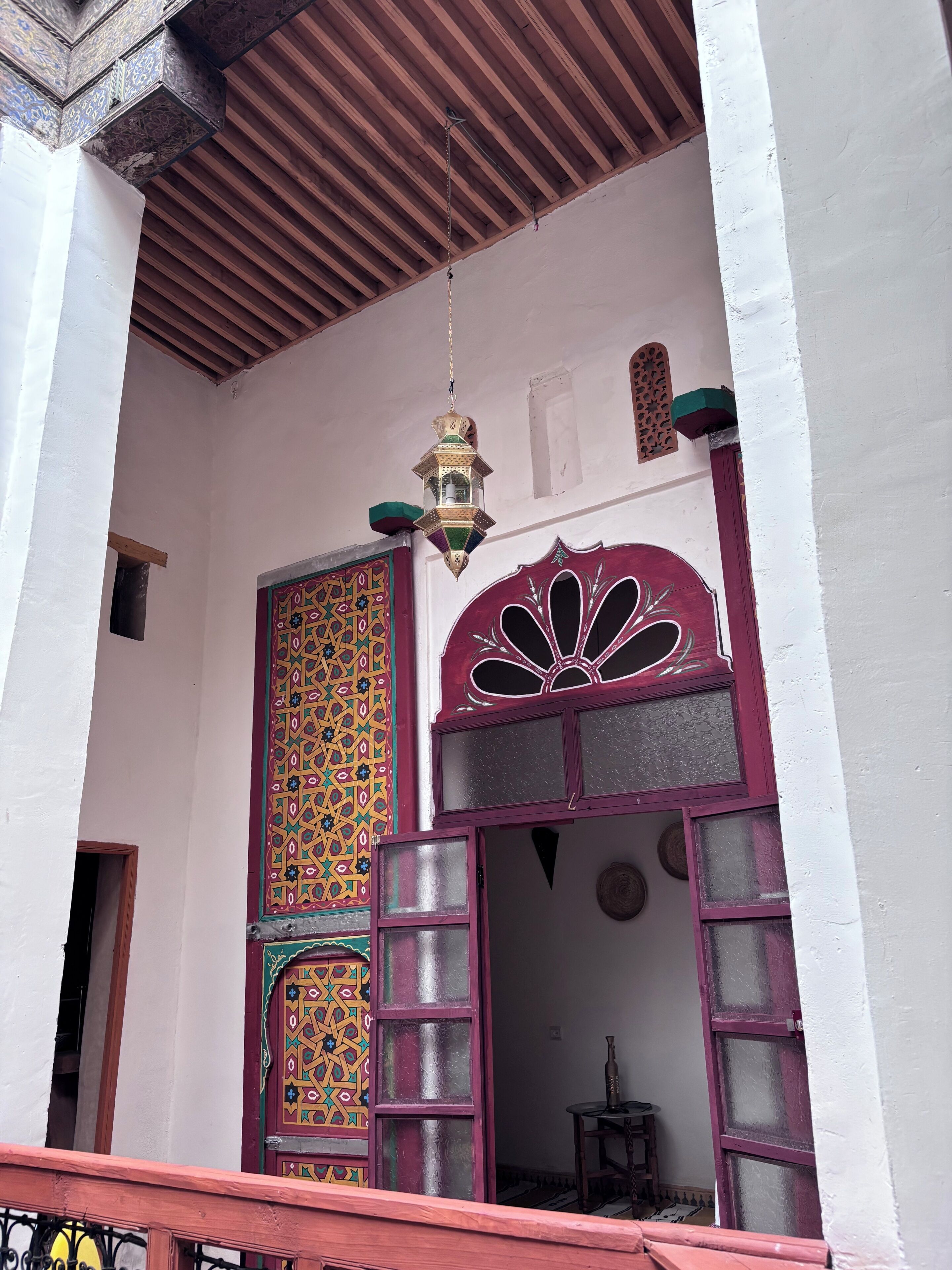 A traditional Moroccan architectural style entrance with a decorative door, a hanging lantern, and a wooden ceiling.