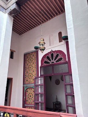 A traditional Moroccan architectural style entrance with a decorative door, a hanging lantern, and a wooden ceiling.