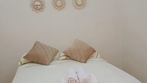 Un llit ben fet amb dues almoines i tovalloles arremolinades, una paret sense decorar amb tres aplics murals, i un paviment amb dibuixos.