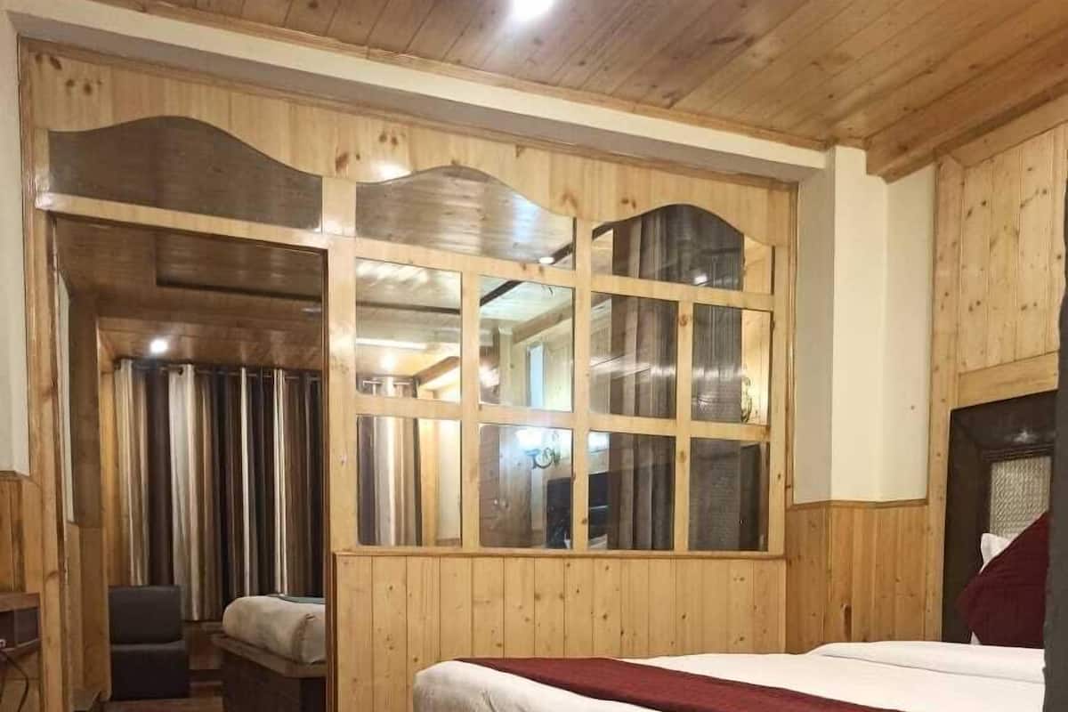 A wooden-paneled room with a large bed, a small seating area, and a view through a window.