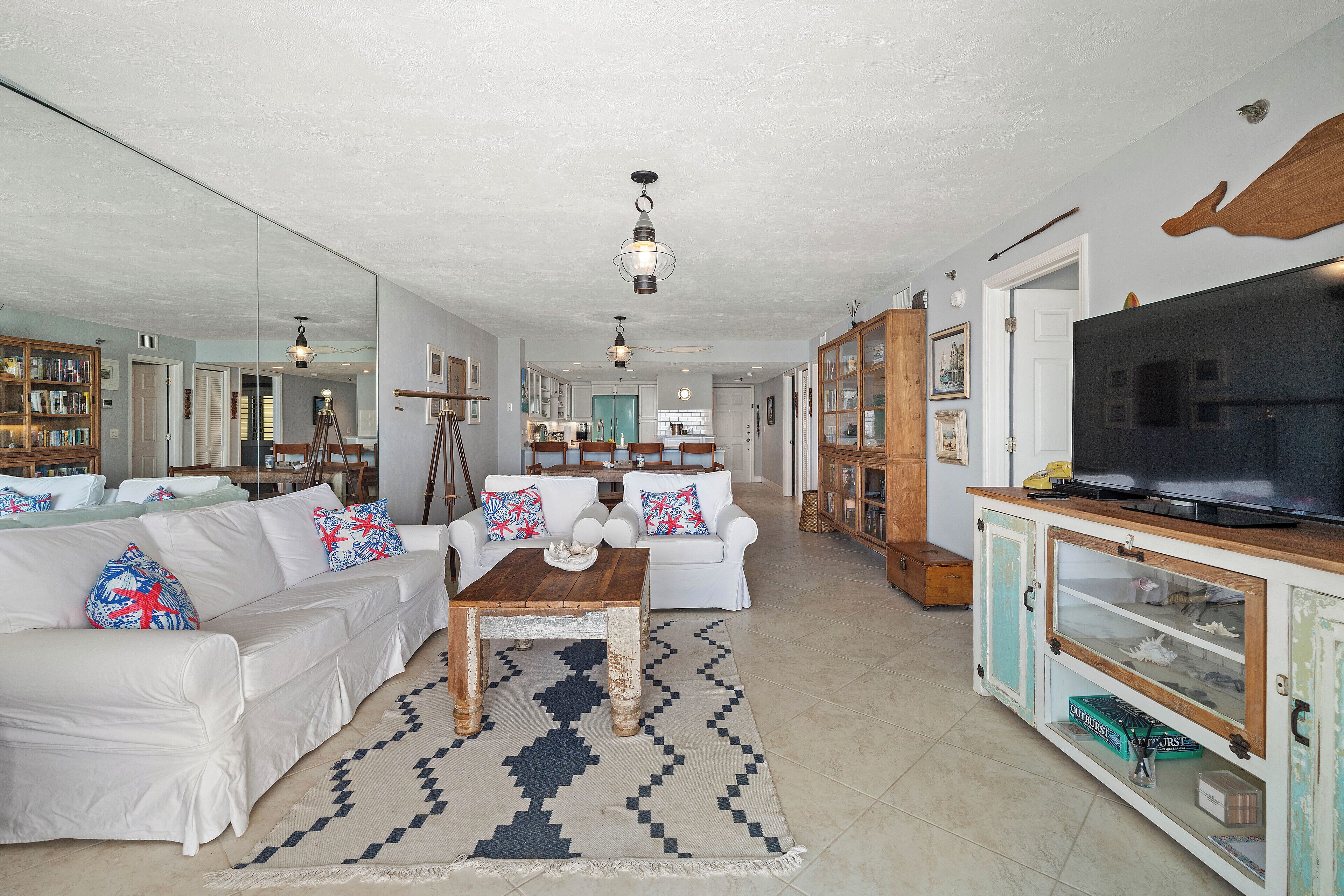 A spacious living room with a white sofa set, a wooden coffee table, and a large TV on a cabinet.