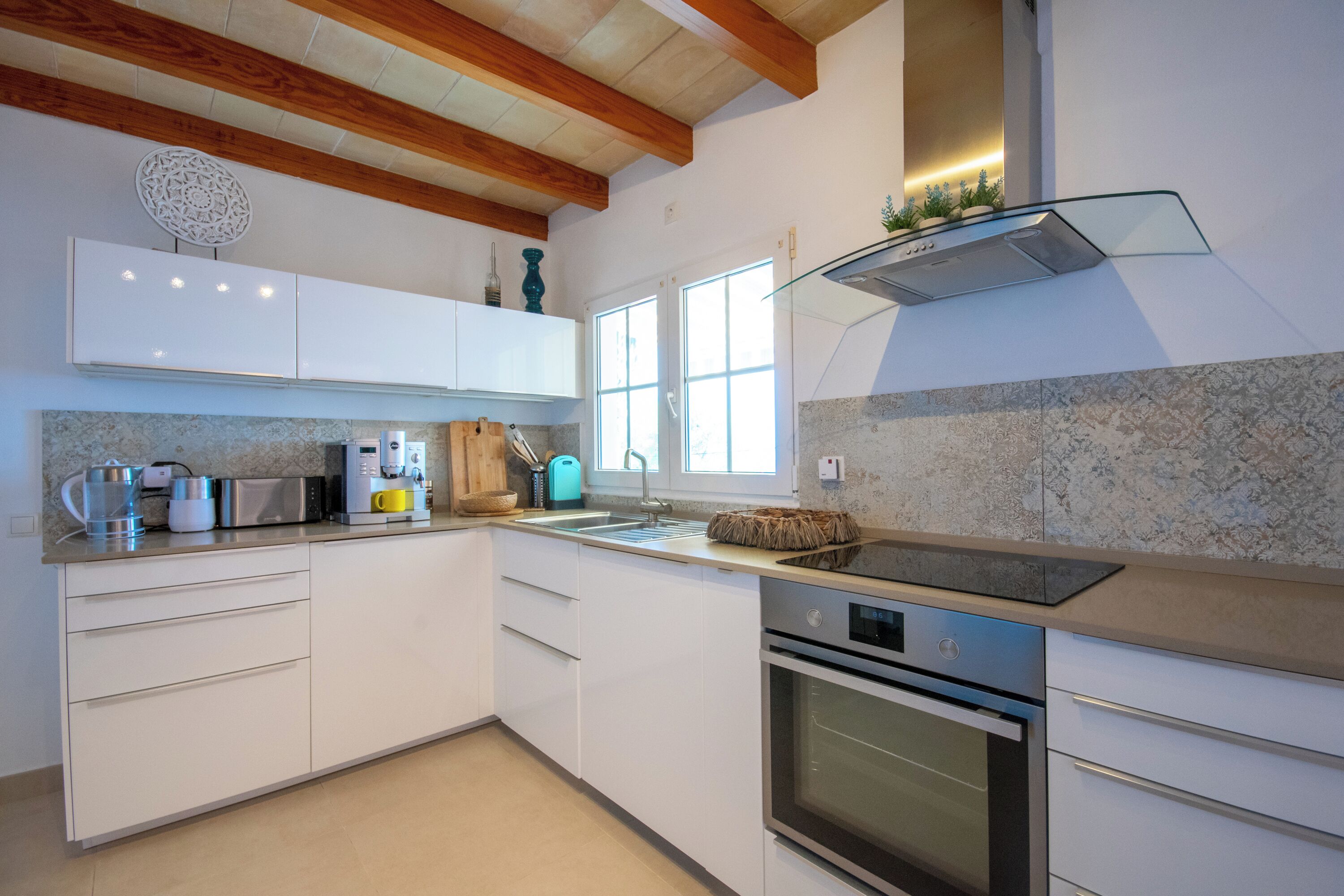 Una cocina moderna con armarios blancos, horno empotrado, microondas y placa vitrocerámica.