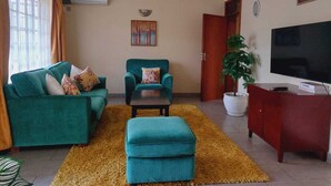 Una sala de estar con sofá, sillón, reposapiés, televisor y planta en maceta.