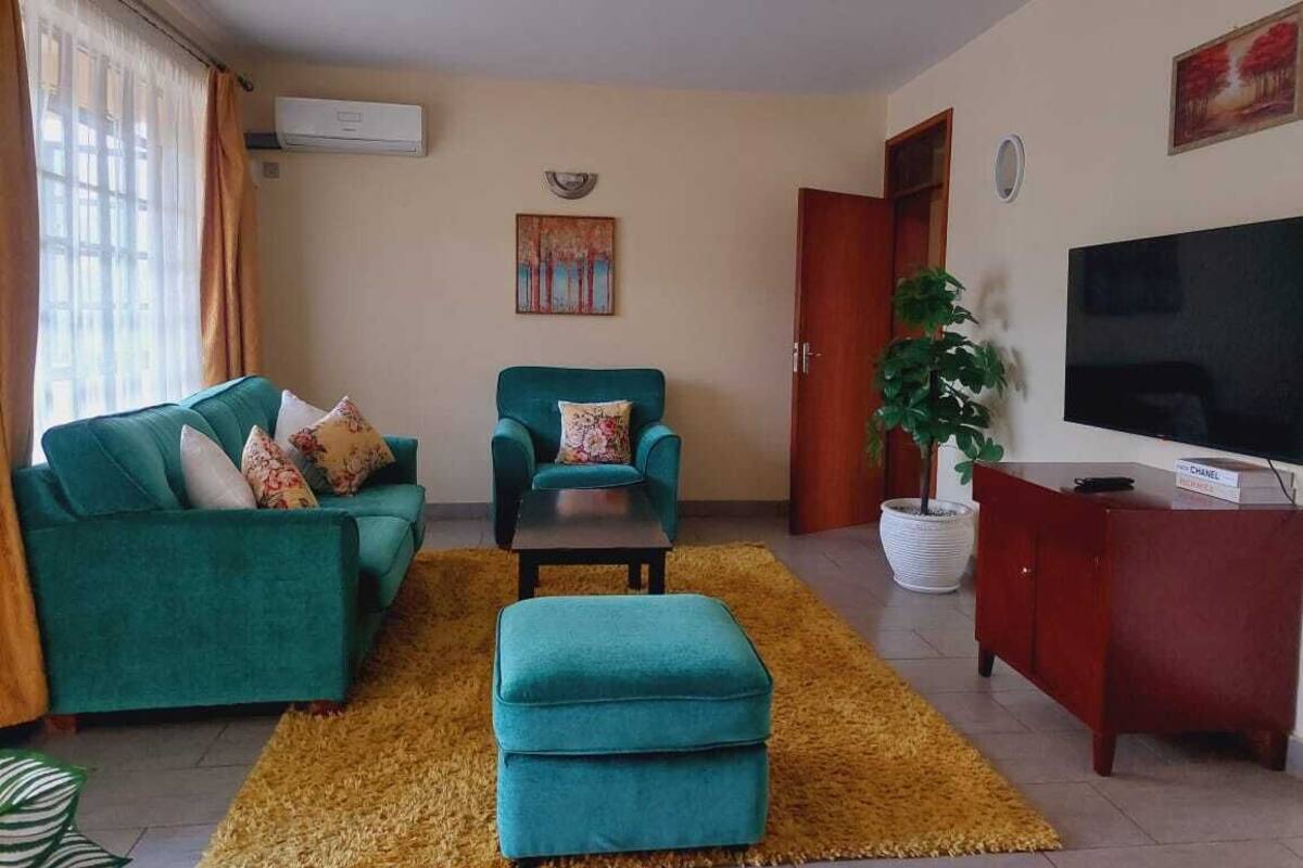 A living room with a sofa, armchair, ottoman, TV, and a potted plant.