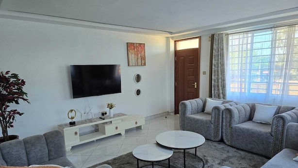 Una sala de estar moderna con sofás grises, un televisor de pantalla plana, una mesa de centro y una planta en maceta.