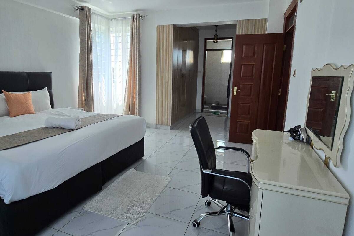 A hotel room with a bed, a desk, a chair, and a door.