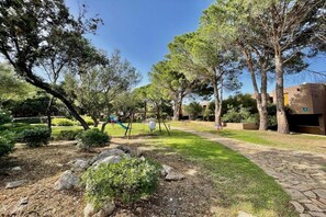 Um parque com parquinho, caminho de pedra e árvores.