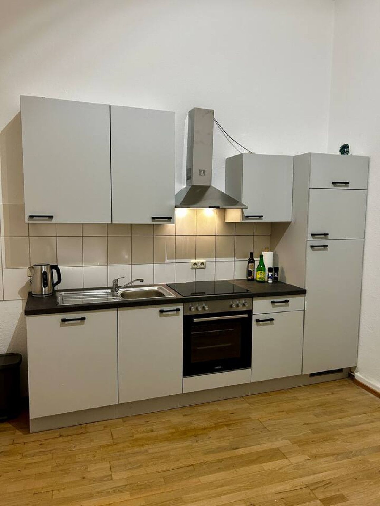 Une cuisine de taille réduite avec des meubles blancs, un plan de travail noir, une cuisinière et un évier.