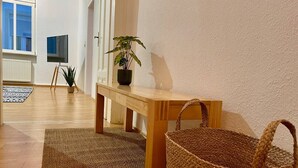Una habitación con una mesa de madera, una cesta tejida, una planta en maceta y un televisor sobre un mueble.