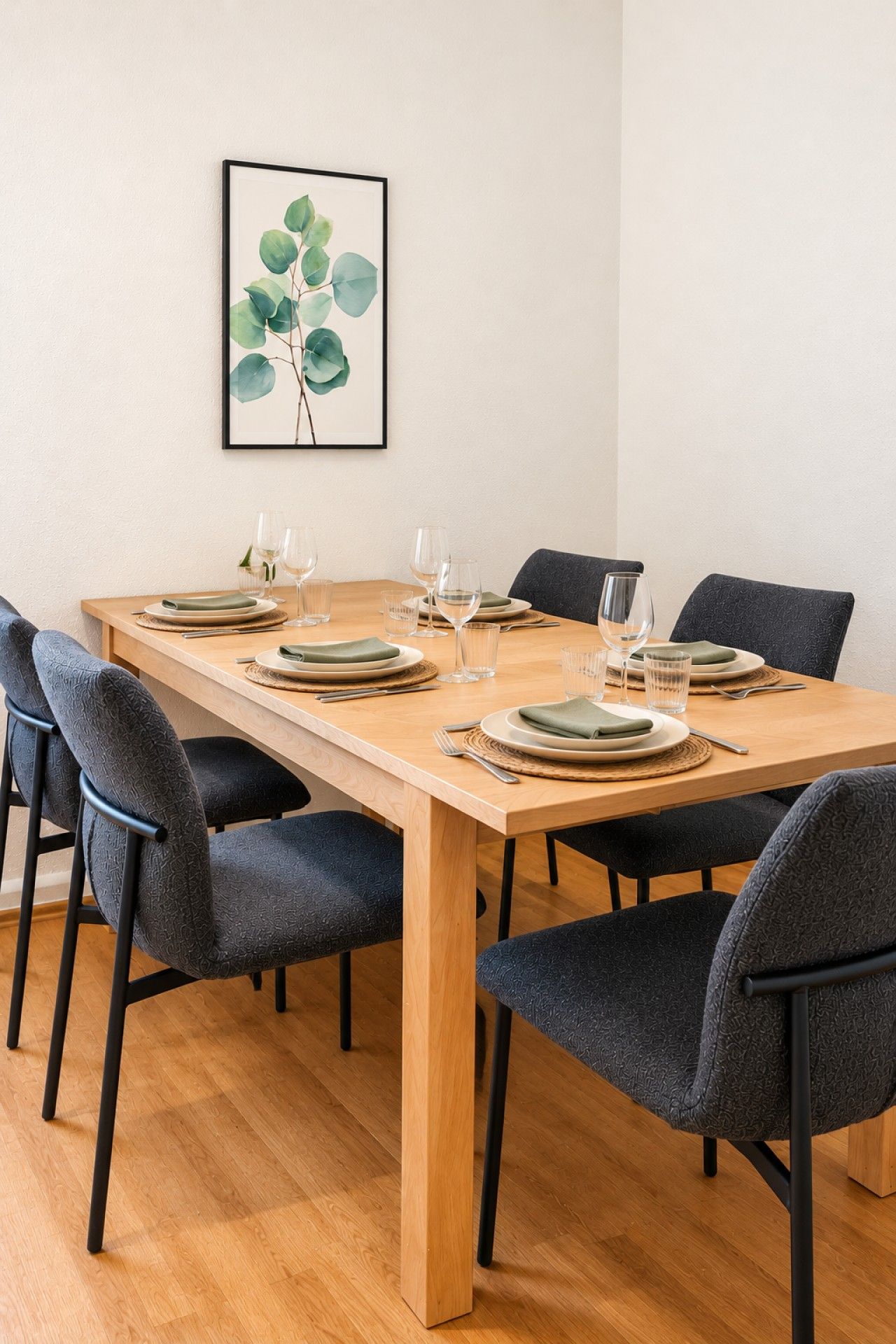 Ein Esstisch ist für sechs Personen gedeckt, mit Stühlen, einem gerahmten Pflanzenprint an der Wand und Holzdielenboden.