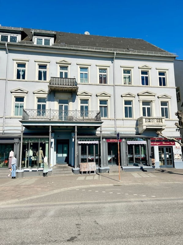En byggnad med flera våningar, en central entré, stora fönster och en balkong på andra våningen.