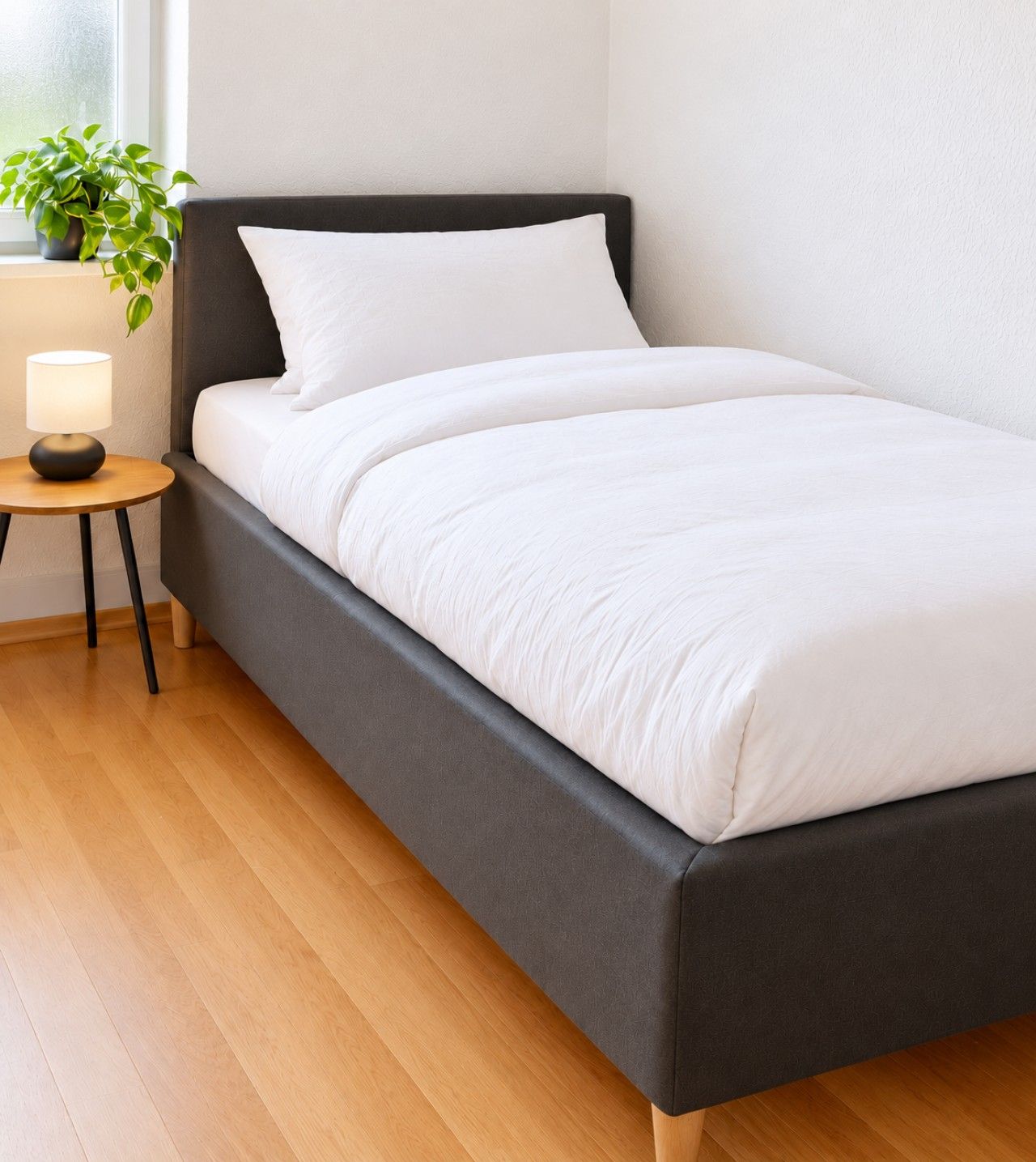 A modern bedroom with a bed, a bedside table with a lamp, and a potted plant.