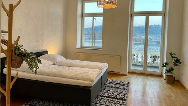 Un dormitorio con cama, ventana, lámpara colgante y vistas al exterior.