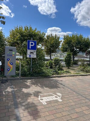 Un panneau de signalisation indiquant un espace de stationnement équipé d’une borne de recharge, d’un panneau solaire et d’un revêtement de pavé en briques.