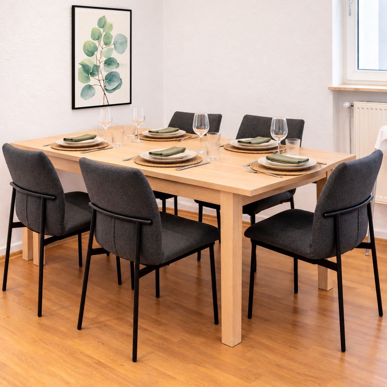 Ett matbord med plats för fyra personer, stolar, en inramad växt på väggen och ett fönster med persienner.