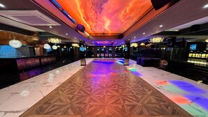 Un hall d’hôtel doté d’un tapis aux motifs géométriques, d’un plafond orné d’un décor représentant un coucher de soleil et de lustres.